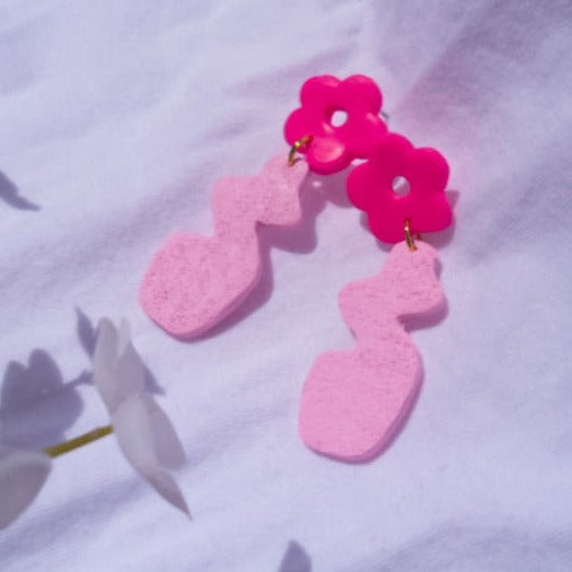 neon pink flower connected to a baby pink flower vase earring. there is a carpet like texture on the vase while the flower is smooth.